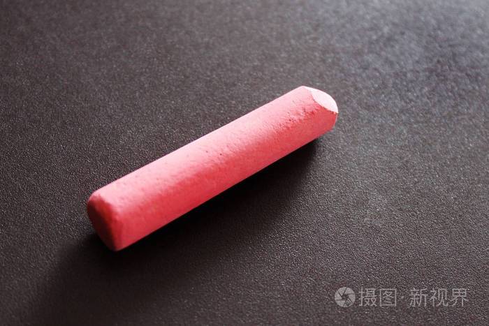 一支粉红色的粉笔躺在磁性板的棕色背景上,投下一个阴影